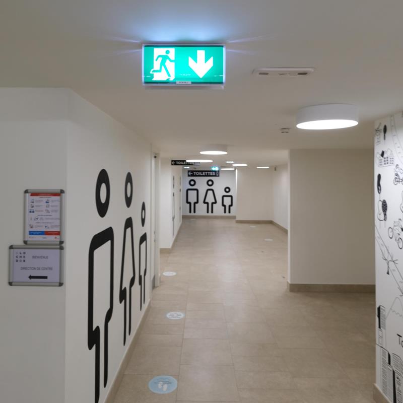 LED-Notleuchte mit Pfeil nach unten an der Decke, Flur mit runden Deckenleuchten