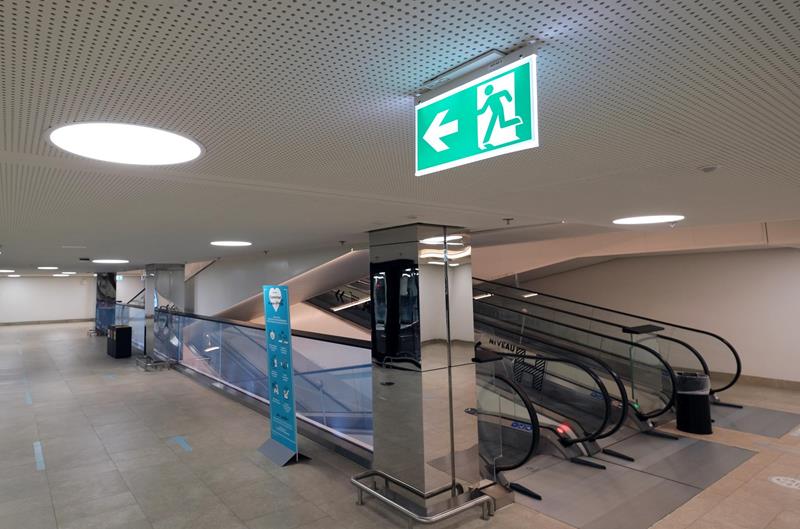 LED-Notausgangsleuchte mit Pfeil links an der Decke, Rolltreppenbereich mit Einbaudownlights